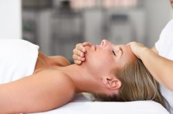 Young blond woman receiving a head massage in a spa center with eyes closed. Female patient is receiving treatment by professional therapist.